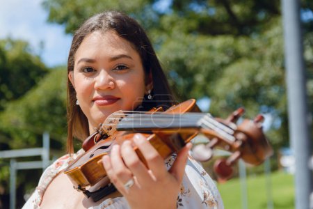 Porträt einer lateinamerikanischen Geigerin, die auf der Straße vor der Kamera steht, während sie mit ihrer Geige arbeitet und stehend mit ihrem Instrument posiert. Musikkonzept, Kopierraum.