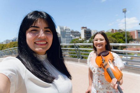 selfie photo of venezuelan latina tourist woman standing on street in venezuela city with violinist busker woman on street smiling looking at camera, lifestyles concept.