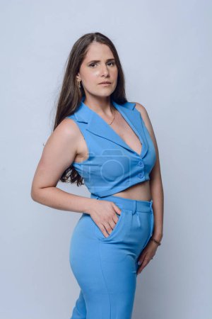 Photo for Young Latina woman of Venezuelan ethnicity, with long brown hair, fashionably dressed in blue executive style clothes standing posing looking at camera, studio shot, copy space. - Royalty Free Image