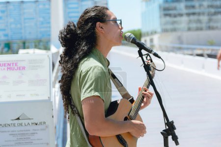profile view of young busker man with long curly hair with sunglasses, in Argentina playing guitar and singing working at noon, copy space.