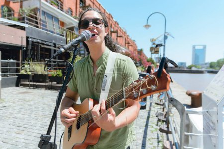 front view of young Venezuelan latin guitarist, on street making music playing and singing working on street in Buenos Aires, working as street artist. copy space