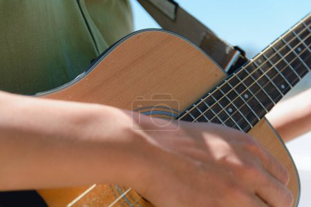 Photo for Closeup of young caucasian man playing acoustic guitar on street at noon, copy space, music concept. - Royalty Free Image