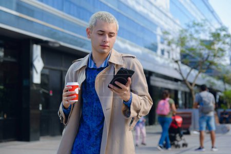 young blond latin university man, in formal clothes, standing checking his phone outside university, browsing internet checking social networks, copy space.