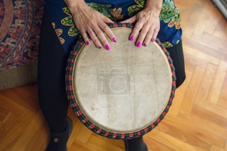 Top view of Female hands on leather head of Djembe drum of a unrecognizable woman sitting playing at home practicing. with the floor on background.