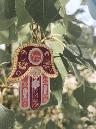Photo for Hamsa hand amulet (hand of Fatima or hand of Miriam) on a background of green leaves closeup. Pink-purple metal pendant Jewish "Hand of Miriam" with the inscription "good luck" outdoors - Royalty Free Image