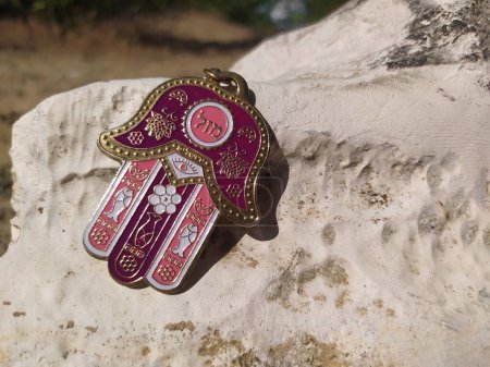 Photo for Hamsa hand amulet with the inscription "Luck" on stone close-up. Pink-purple Jewish "Hand of Miriam" close-up outdoors. Hamsa is the popular protection amulet - Royalty Free Image