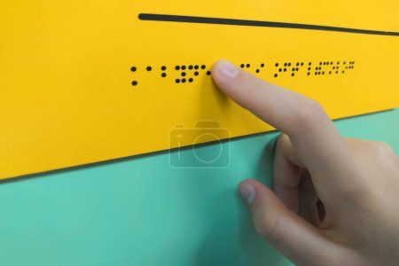 Close-up of a woman's hand reading the word "ophthalmologist" in Braille. The concept of the day of the blind and disabled. World Sight Day. World Braille Day. The child hand is touching the convexity of the plate. Blind and partially sighted people