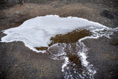 Foto de Espuma jabonosa blanca en agua sucia gris en un charco en el suelo exterior - Imagen libre de derechos
