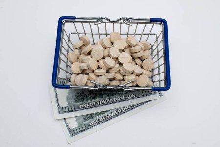 Photo for Multivitamin tablets in shopping basket with dollar bills on white background - Royalty Free Image
