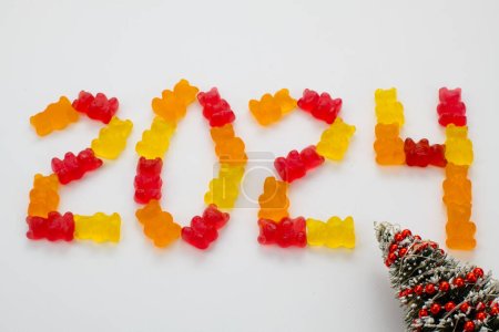 Happy New Year 2024 with Colorful design. With Year 2024 laid out from round multicolored gummy bears and christmas tree