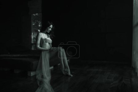 black and white portrait model asian women naked sitting with some white cloth in dark room, emotion of art natural light and shadow concept 