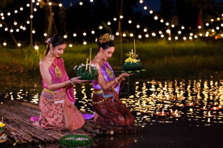 Loi Krathong Festival, Zwei thailändische Frauen mit einem Krathong auf einem Floß am Fluss, asiatische Frauen in traditionellen thailändischen Kostümen bringen Krathongs zum Loi Krathong Day, Traditionen und Kultur Thailands,