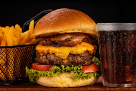 Hamburger accompanied by fries and soda in a studio photo with brown and black wood