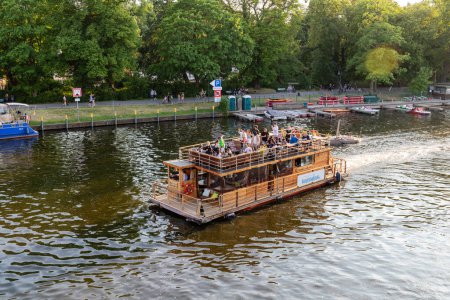 Foto de Berlin-Treptow, Alemania - 9 de junio de 2023, Vista del Spree con restaurantes y varios alquileres de barcos en Treptower Park. Los barcos de excursión van en el río, espacio de copia. - Imagen libre de derechos