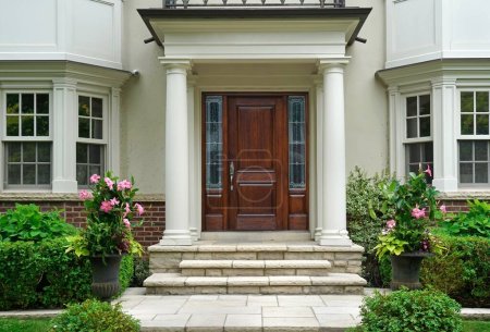 Élégante porte avant en bois de grain de maison avec entrée portique entourée de fleurs et d'arbustes