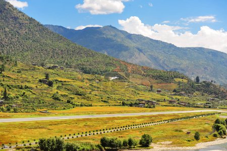 Foto de Una vista panorámica del aeropuerto y el valle del Paro, Bután. Paisaje con Montaña, río, prados verdes y tierras agrícolas, cielo azul con nubes blancas. - Imagen libre de derechos