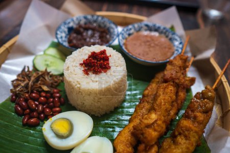 Asiatisches Essen Nasi Lemak ist ein Reisgericht, das mit Kokosmilch getränkt wird. Serviert mit Sambal, gebratenen Sardellen, gebratenen Erdnüssen, gekochten Eiern und frischen Gurken. Hochwertiges Foto