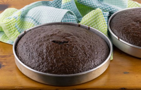 Unfrosted chocolate cakes in pans on wooden table - selective focus