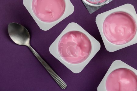 Fruit flavoured yogurt in white plastic cups on bright purple background with silver foil lid - Overhead photo of yoghurt cup background with selective focus