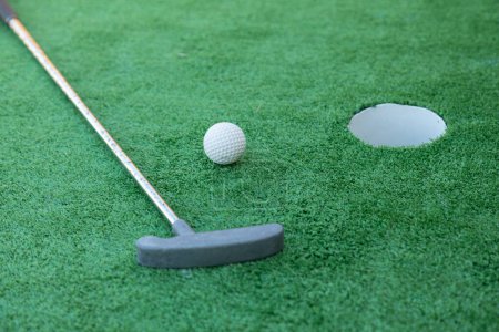 Equipo de mini golf, club de golf, pelota y hoyo en terreno verde 