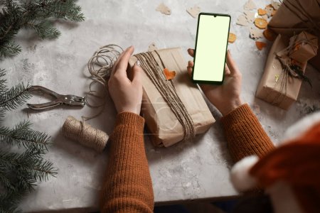 une jeune femme tient un téléphone, une tablette à la main et remplit une commande par téléphone, prenant une commande pour emballage cadeau, en arrière-plan un arbre de Noël et des lumières, le concept de préparation pour la nouvelle année, joyeux Noël, nouvel an 2023