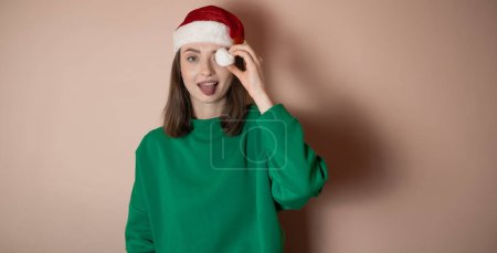 Téléchargez les photos : Jeune femme dans un chapeau du Nouvel An, une femme montre sa langue, couvert son oeil avec un pompon d'un chapeau, le concept de préparation pour la nouvelle année, joyeux Noël, nouvelle année 2023, fille heureuse, fond monochrome, clé chromée - en image libre de droit