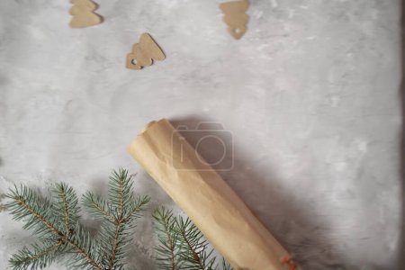 Téléchargez les photos : Emballage des cadeaux du Nouvel An, branches de sapin et papier d'emballage artisanal se trouvent sur la table, papier d'emballage sur un fond gris, arbres de Noël en papier, préparation pour Noël, concept d'emballage cadeau - en image libre de droit