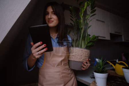 Eine Frau mit einem Tablet dokumentiert Zimmerpflanzen und zeigt ihre Leidenschaft für die Gartenarbeit und das Pflanzen von Blumen zu Hause. Dieses Bild fängt die Essenz wachsender Zimmerpflanzen und die Freude am Wachsen in Innenräumen ein.
