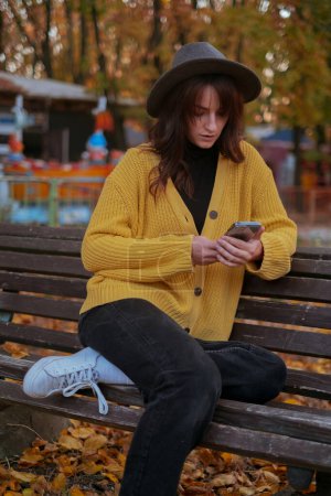 Una viajera trabaja al aire libre, sosteniendo un teléfono, en un parque de otoño.