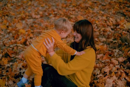 Una madre y un hijo pasan tiempo de calidad juntos, jugando en el parque de otoño, ambos vestidos con atuendo amarillo. En medio del colorido follaje, comparten momentos alegres, risas resonando en el aire crujiente.