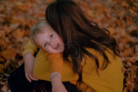 A mother and son embrace and kiss, enjoying a family weekend in the autumn park, surrounded by the warmth of their love.
