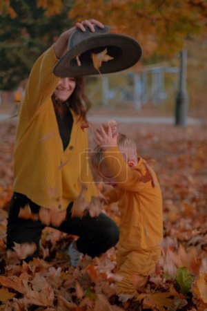 A mother and son spend quality time together, playing in the autumn park, both dressed in yellow attire. Amidst the colorful foliage, they share joyful moments, laughter echoing in the crisp air.