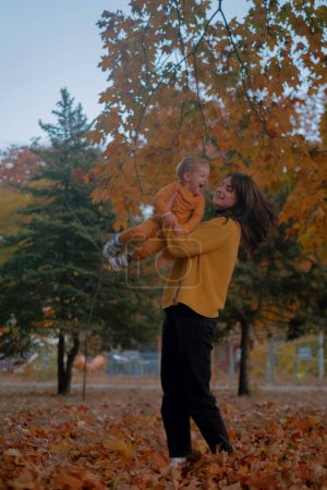 A mother and son spend quality time together, playing in the autumn park, both dressed in yellow attire. Amidst the colorful foliage, they share joyful moments, laughter echoing in the crisp air.