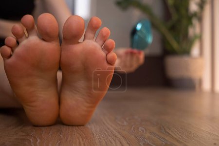 Primer plano de los pies de una mujer con piel callosa y callos, utilizando una lima para pedicura, rutina de cuidado de los pies en casa.