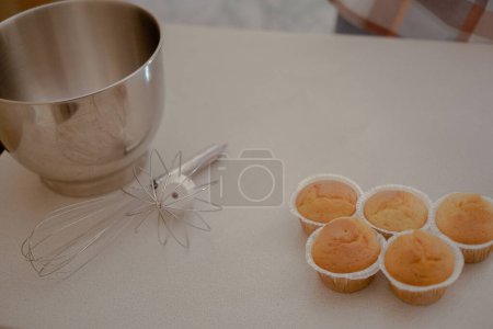 Sur la table se trouvent des cupcakes, mettant en valeur l'art d'une pâtissière. La table de cuisine présente les outils et ingrédients d'un chef pâtissier, prêt pour les créations culinaires.