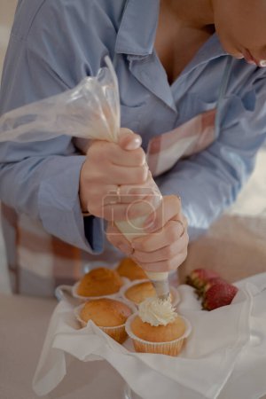 Foto de Una hembra de pastelería pipa glaseado en cupcakes, mostrando sus productos horneados caseros. Explore el encanto de la panadería casera y la pequeña empresa con esta imagen de un panadero experto en el trabajo. - Imagen libre de derechos