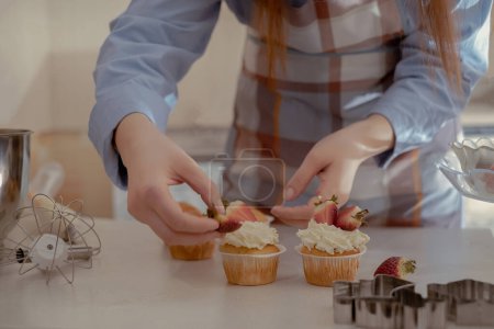 Une pâtissière décore les cupcakes avec des baies, mettant en valeur ses pâtisseries maison. Explorez le charme de la boulangerie maison et des petites entreprises avec cette image d'un boulanger qualifié au travail.