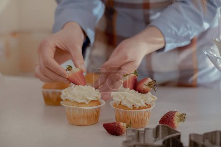 Une pâtissière décore les cupcakes avec des baies, mettant en valeur ses pâtisseries maison. Explorez le charme de la boulangerie maison et des petites entreprises avec cette image d'un boulanger qualifié au travail.