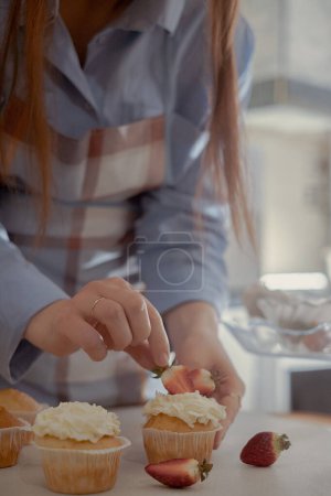 A female pastry chef decorates cupcakes with berries, showcasing her homemade baked goods. Explore the charm of home baking and small-scale business with this image of a skilled baker at work.