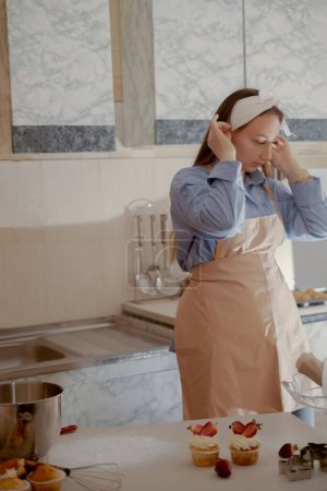 A female baker ties her apron in the kitchen, preparing to bake cupcakes. Get ready for some homemade sweetness with this kitchen scene of a home baker.