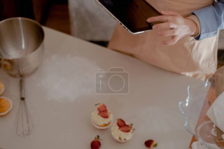 Foto de Una chef de pastelería femenina tiene una tableta para gestionar los pedidos, que representa la cocción casera. Experimente la esencia de hornear a pequeña escala y respetuoso del medio ambiente con productos sin gluten y sin azúcar, promoviendo una alimentación saludable. - Imagen libre de derechos