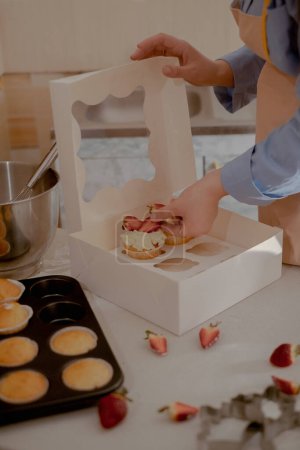 Eine Konditorin verpackt Cupcakes in Verpackungen für den Versand an Kunden und präsentiert hausgemachtes Backen. Erleben Sie die Essenz des kleinen, umweltfreundlichen Backens mit gluten- und zuckerfreien Produkten und fördern Sie eine gesunde Ernährung.