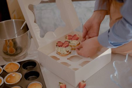 A female pastry chef packs cupcakes into packaging for shipping to customers, showcasing homemade baking. Experience the essence of small-scale, eco-friendly baking with gluten-free and sugar-free products, promoting healthy eating.