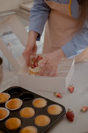 A female pastry chef packs cupcakes into packaging for shipping to customers, showcasing homemade baking. Experience the essence of small-scale, eco-friendly baking with gluten-free and sugar-free products, promoting healthy eating.
