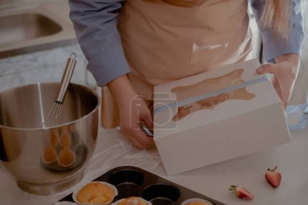 Un chef pâtissier féminin emballe les cupcakes dans un emballage pour les expédier aux clients, mettant en valeur la cuisson artisanale. Découvrez l'essence de la cuisson écologique à petite échelle avec des produits sans gluten et sans sucre, en promouvant une alimentation saine.