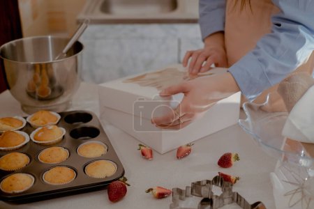 Una chef de pastelería empaca cupcakes en envases para enviar a los clientes, mostrando hornear en casa. Experimente la esencia de hornear a pequeña escala y respetuoso del medio ambiente con productos sin gluten y sin azúcar, promoviendo una alimentación saludable.