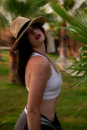 Chica en sombrero de paja pasea por la playa entre palmeras, encarnando vibraciones de vacaciones. Perfecto para destinos de viaje, paquetes turísticos y marcas de moda de ropa de playa.