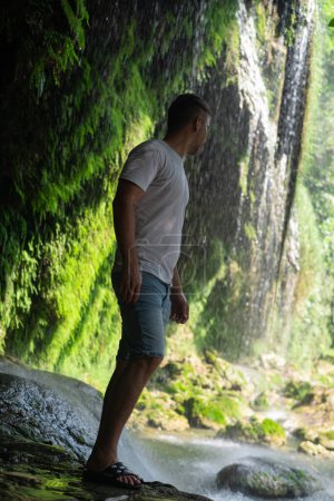 Man marvels at waterfall in nature reserve, ideal for tourism, excursions, adventure tours, extreme leisure, national parks, and reserves.