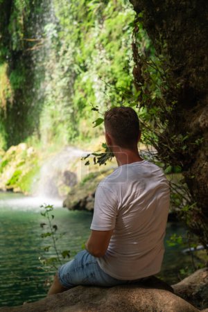 Man marvels at waterfall in nature reserve, ideal for tourism, excursions, adventure tours, extreme leisure, national parks, and reserves.