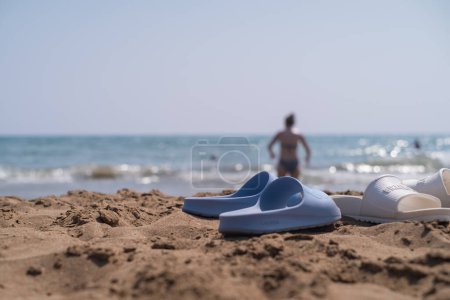 Sandales de plage au bord de la mer, vagues s'écrasant contre le sable jaune, vente de chaussures et accessoires de plage, stations touristiques et plages.